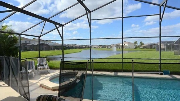 A pool area with a view of a golf course, enclosed by a metal structure. - Stunning Waterview Pool Home: Gated, 4BR, Outdoor Spa, Games Room, Free WiFi! (Kissimmee)