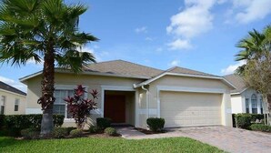 A single-story house with a garage, a well-maintained lawn, and a palm tree. - Stunning Waterview Pool Home: Gated, 4BR, Outdoor Spa, Games Room, Free WiFi! (Kissimmee)