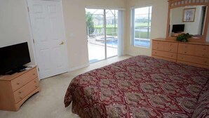 A bedroom with a large bed, a television on a dresser, and a sliding glass door leading to a patio with a pool. - Stunning Waterview Pool Home: Gated, 4BR, Outdoor Spa, Games Room, Free WiFi! (Kissimmee)