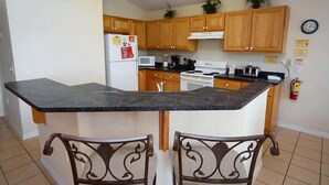 A kitchen with wooden cabinets, a black countertop, a stove, and a refrigerator. - Stunning Waterview Pool Home: Gated, 4BR, Outdoor Spa, Games Room, Free WiFi! (Kissimmee)