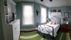 A bedroom with a bed, a dresser, a nightstand, a lamp, a shelf with decorative items, and a window with blinds. - Lancaster City home with fenced yard and off street parking, walk to downtown (Lancaster)