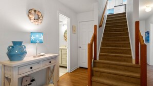 A staircase with wooden railings leading to a second floor, a white door, and a wall-mounted wreath.