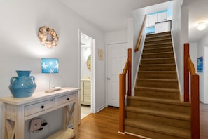 Eine Treppe mit hölzernen Geländern, die zu einer zweiten Etage führt, eine weiße Tür und ein an der Wand befestigter Kranz.