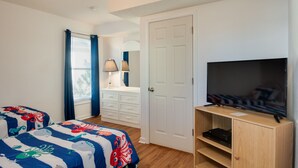 A bedroom with two beds, a TV, a desk with a lamp, and a door.