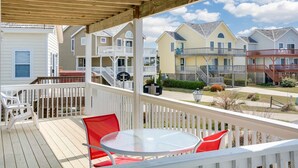 A covered outdoor area with a wooden deck, white railings, and a glass table with red chairs.