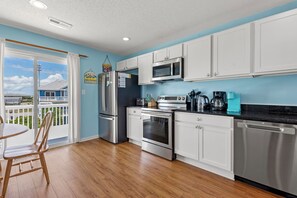 A kitchen with white cabinets, stainless steel appliances, a dining table with chairs, and a view of a balcony.