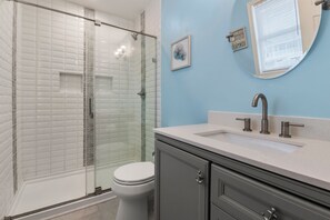 Ein Badezimmer mit Duschkabine aus Glas, einer weißen Toilette, einem Waschbecken mit Spiegel und einem Schrank.