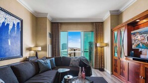A modern hotel room with a large sofa, a small table with drinks, and a view of the city through large windows.