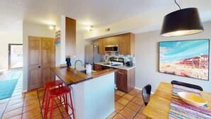 Una cocina moderna con armarios de madera, una isla central, taburetes de bar rojos y una mesa de comedor con un mantel individual colorido.
