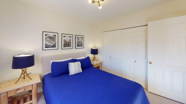 A bedroom with a large bed, two bedside tables with lamps, a wardrobe, and three framed pictures on the wall.