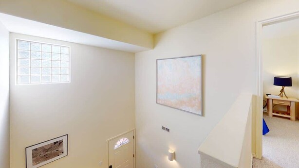 Una habitación con ventana, un cuadro en la pared, una puerta y una pequeña mesa con una lámpara.
