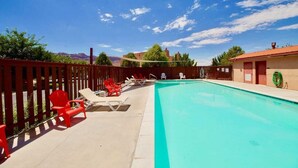 Una piscina con sillas de descanso rojas y blancas, una valla de madera y un edificio con techo rojo al fondo.