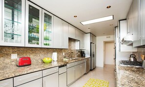 A modern kitchen with granite countertops, stainless steel appliances, and glass-front cabinets.