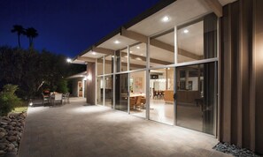A modern house with a patio area, large glass doors leading to an interior space, and a stone pathway.