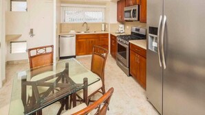 A compact kitchen with wooden cabinets, stainless steel appliances, and a glass dining table. - Airy, Casual Ocean View Suite w/Upgraded Kitchen, Free WiFi-Waikīkī Shore 1406 (HONOLULU)