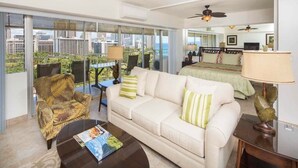 A hotel room with a large window, a sofa, a coffee table, a chair, a bed, and a ceiling fan. - Airy, Casual Ocean View Suite w/Upgraded Kitchen, Free WiFi-Waikīkī Shore 1406 (HONOLULU)