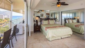 A balcony with a view of the sea and buildings, a bed with a canopy, a ceiling fan, and a small table with a lamp. - Airy, Casual Ocean View Suite w/Upgraded Kitchen, Free WiFi-Waikīkī Shore 1406 (HONOLULU)