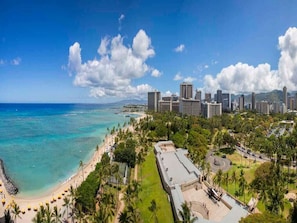 Paisagem costeira com praia, palmeiras e uma combinação de edifícios modernos e antigos.