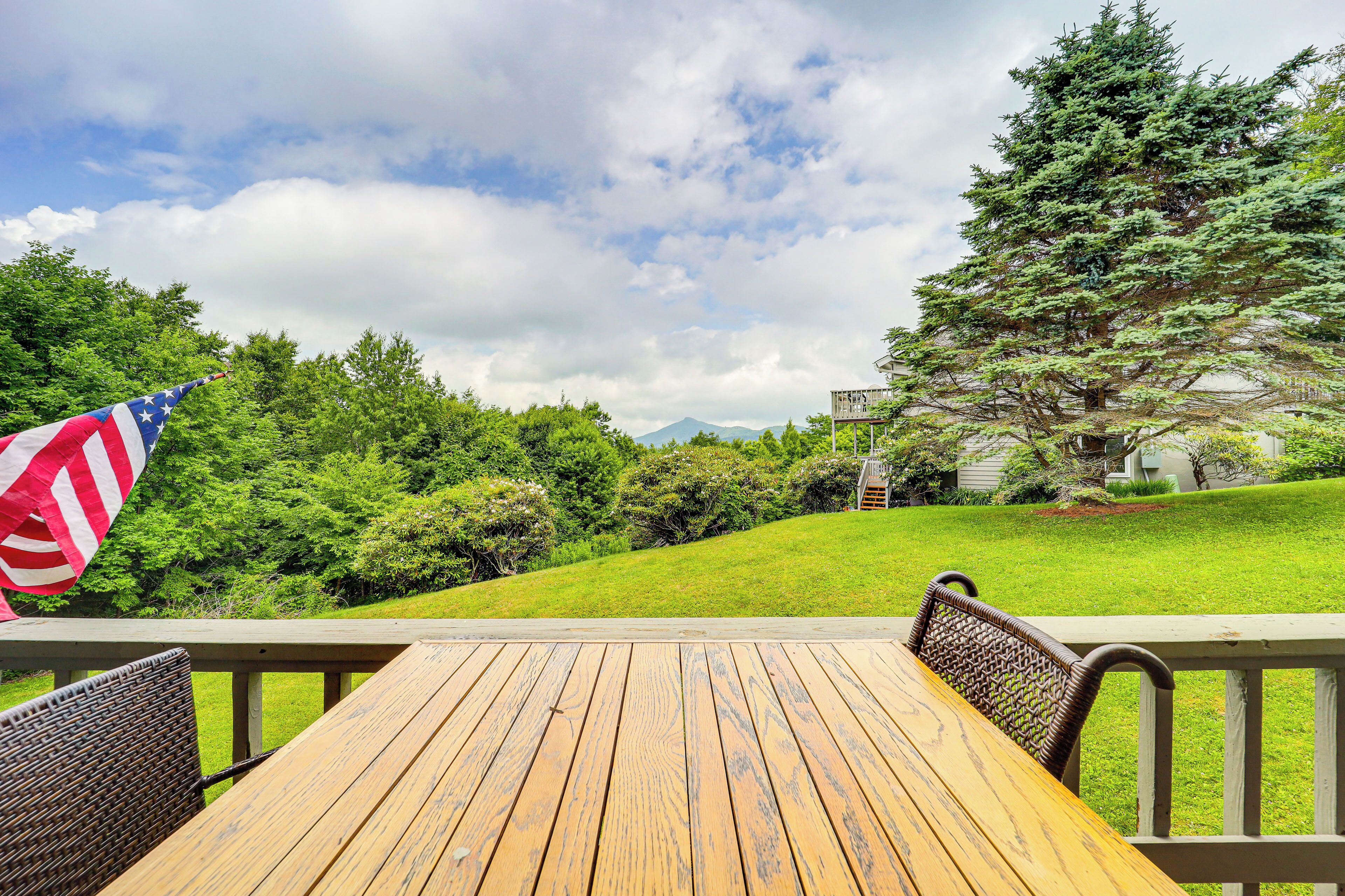 Eine Holzdar Terrasse mit Tisch und Stühlen, mit Blick auf eine Rasenfläche mit Bäumen und einem Berg in der Ferne.