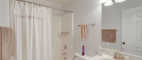 A bathroom with a shower, toilet, sink, and a mirror.