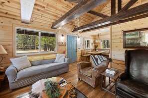 Ein gemütliches Blockhaus-Interieur mit einer Couch, einem Sessel und einem Esstisch.