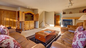 A living room with a leather sofa, a wooden cabinet, a fireplace, and a staircase. - Spacious Home: Hot Tub, Serene Forest (Breckenridge)