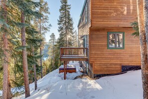 Une cabane en bois dotée d’un balcon, entourée de grands pins et bordée d’un sol enneigé.