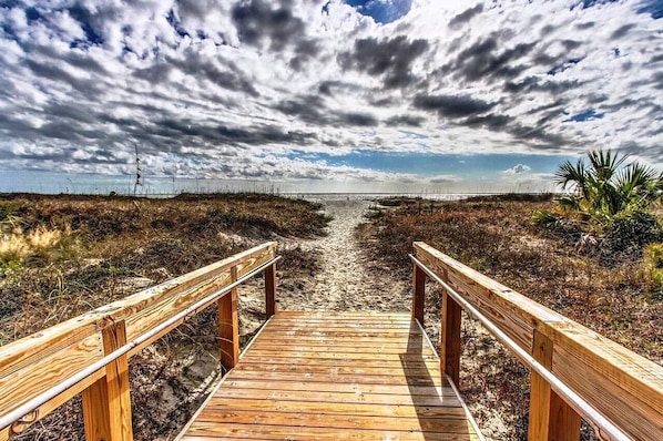 A wooden boardwalk leading to a beach with a cloudy sky.