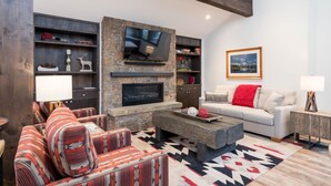 A modern living room with a stone fireplace, a flat-screen TV, and a cozy seating area with patterned cushions.