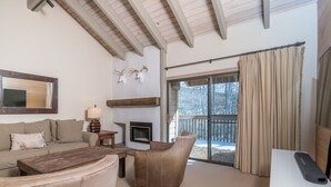 A cozy living room with a fireplace, a sofa, a chair, and a large window with curtains.