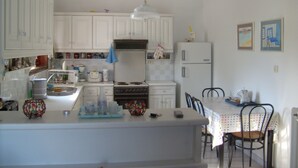 A kitchen with white cabinets, a stove, a refrigerator, and a dining table with chairs. - A BALCONY WITH AMAZING SEA VIEW (CHIOS)