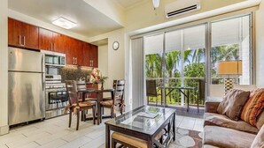 A modern kitchen with stainless steel appliances, a dining area with a glass table, and a balcony with a view of palm trees.