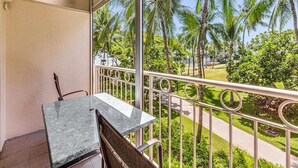 A balcony with a table and chairs, overlooking a garden with palm trees and a pathway.