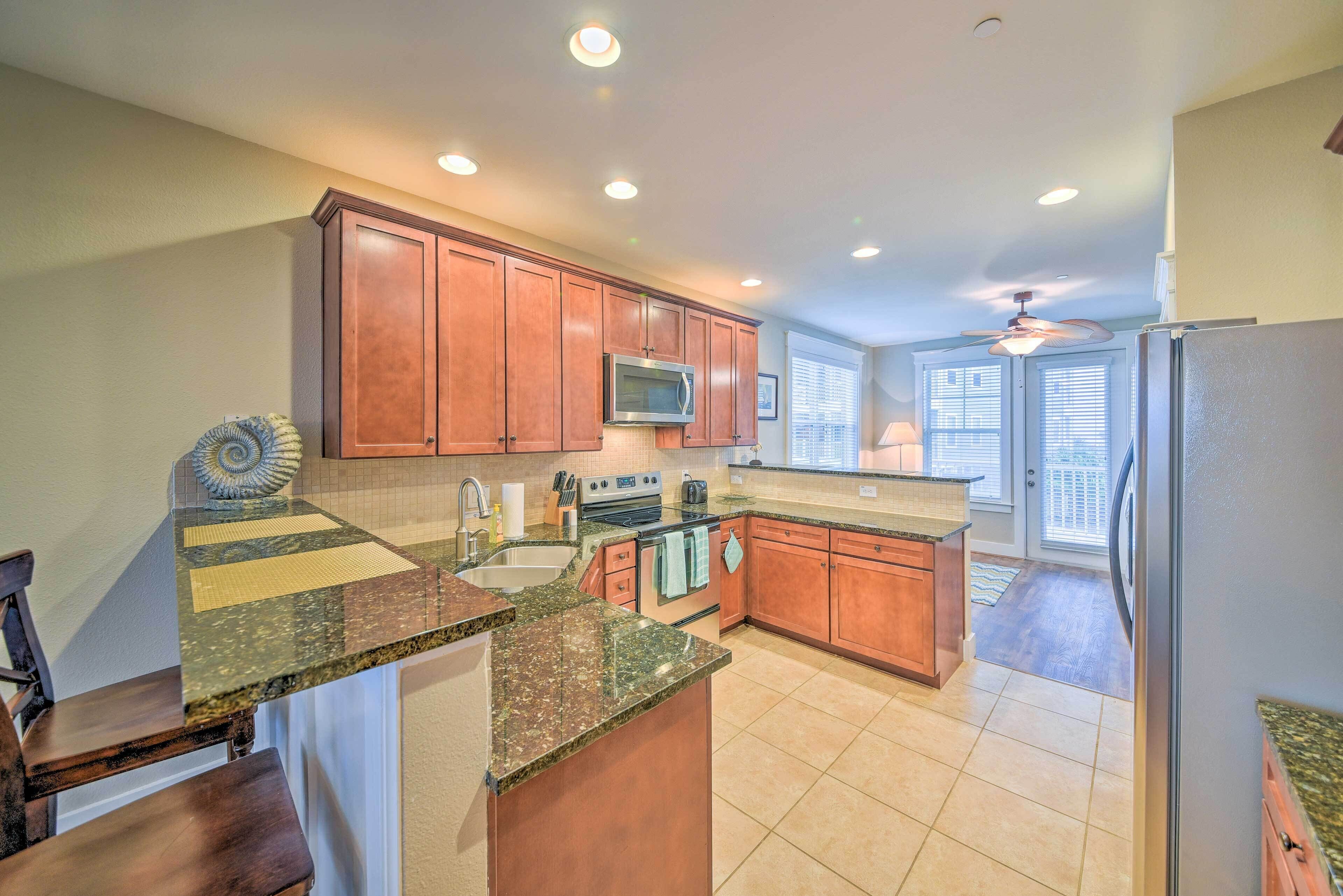 A kitchen with granite countertops, wooden cabinets, a microwave, stove, and a ceiling fan.