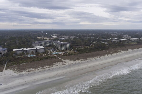 Vista aérea de una zona costera con hoteles frente a la playa, playas de arena y olas del océano.