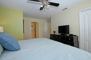 A bedroom with a bed, a ceiling fan, a television on a dresser, and a door.