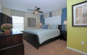A bedroom with a bed, a desk, a chair, a ceiling fan, and a window with blinds.