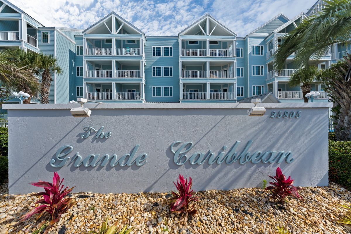 Un immeuble à plusieurs étages doté de balcons, une enseigne indiquant « The Grande Caribbean », et le numéro « 25805 » inscrit sur le mur.