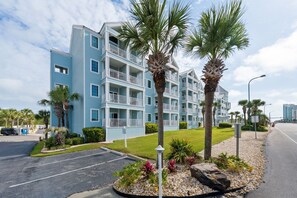A multi-story hotel with balconies, palm trees, and a parking lot.