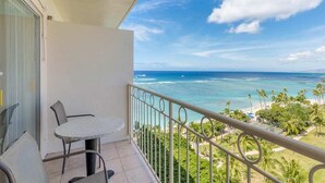 Un balcon avec une table et des chaises, donnant sur une plage bordée de palmiers et sur l’océan.