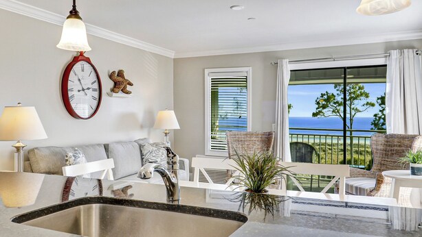 A modern living room with a large window, a kitchen area, and a balcony with a view of the ocean. - Stunning views of the Beach! Gorgeous Oceanfront Heated Pool (Hilton Head Island)