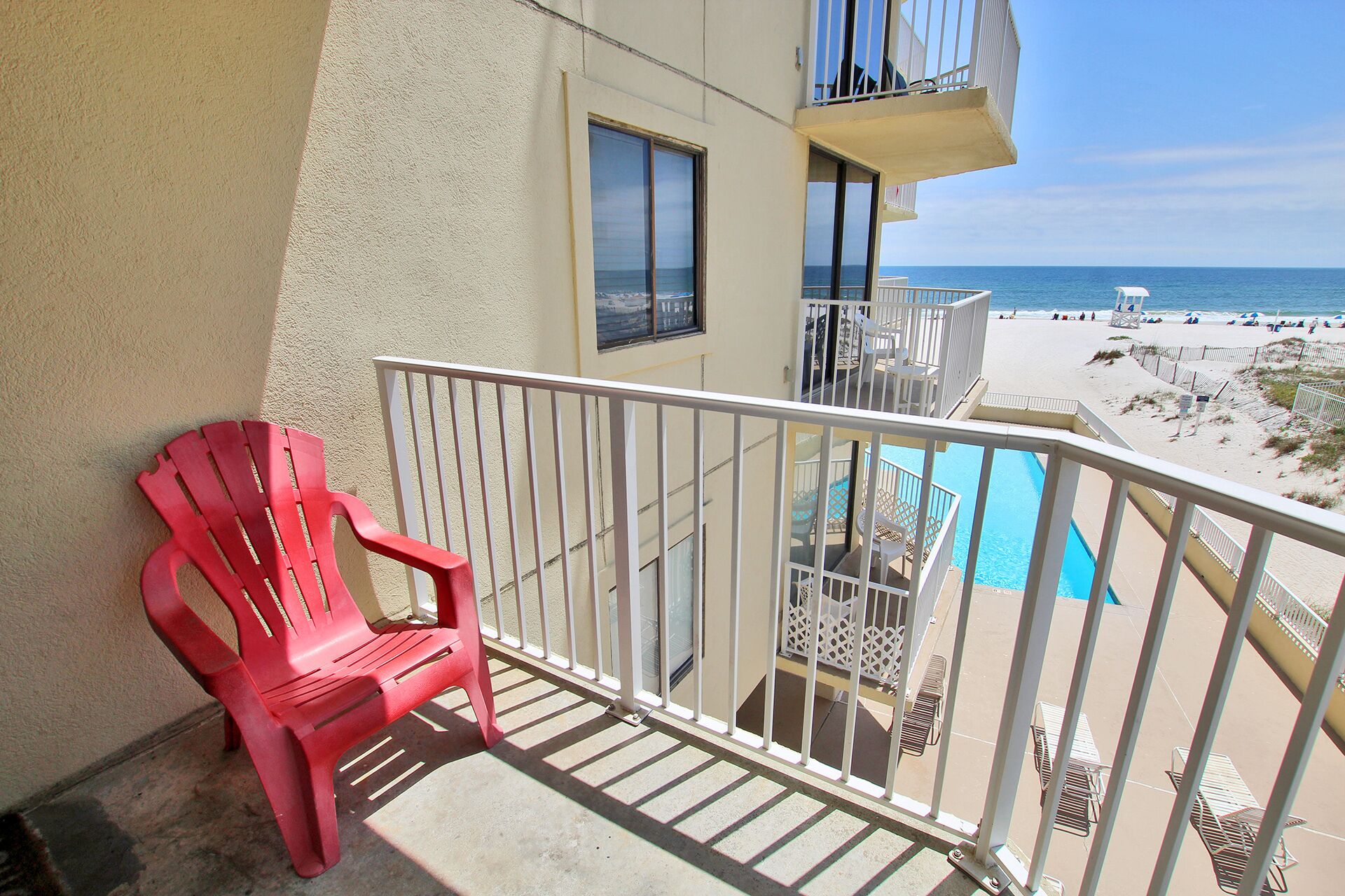 Ein Balkon mit einem roten Stuhl, einem Pool und Blick auf den Strand.