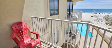Ein Balkon mit einem roten Stuhl, einem Pool und Blick auf den Strand.