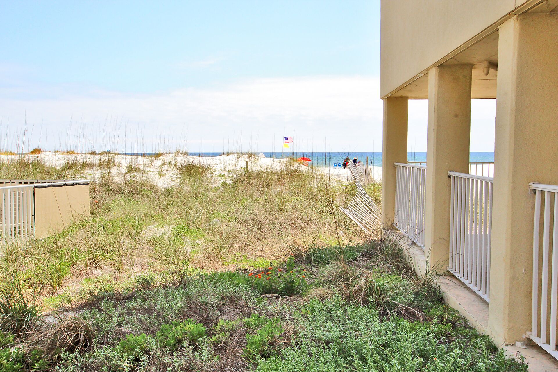 A view of a beach with sand dunes and a flag in the distance.
