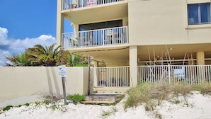 Un immeuble de deux étages doté de balcons, une plage de sable devant, et une enseigne indiquant l’adresse.