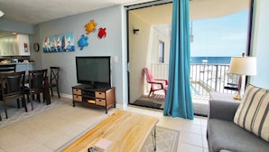 Un salon avec une télévision, une table basse en bois et un canapé. Il y a un balcon avec vue sur la plage.