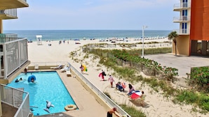 Un espace piscine avec vue sur la plage, un poste de surveillance pour les sauveteurs et un bâtiment doté de balcons.
