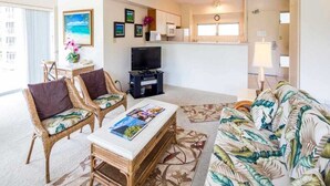 A living room with wicker furniture, a flat-screen TV, and a tropical-themed couch. - Tropical Family Pick w/Kitchen Ease, Free WiFi, Washer/Dryer–Waikīkī Shore 318 (HONOLULU)
