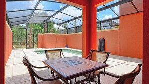 Une terrasse couverte avec une table et des chaises, une piscine et une vue sur les palmiers.
