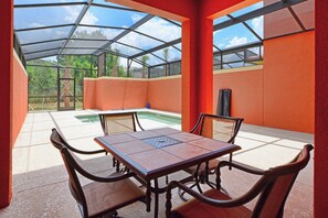 A covered patio with a table and chairs, a pool, and a view of palm trees. - Paradise Palms | Private Splash Pool & BBQ | 2 King Beds | Dog Friendly | Near Disney (Kissimmee)